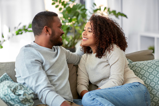 relationships, communication and people concept - happy african american couple sitting on sofa and talking at home