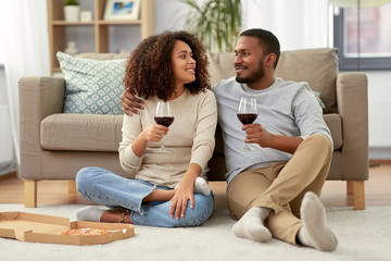 Obraz premium leisure, people and valentines day concept - happy african american couple with wine and takeaway pizza at home