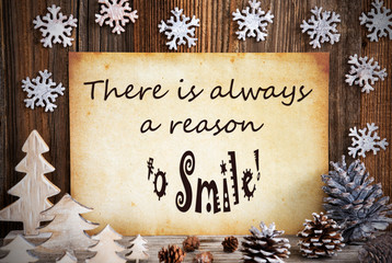 Obraz na płótnie Canvas Old Paper With English Quote There Is Always A Reason To Smile. Christmas Decoration Like Tree, Fir Cone And Snowflakes. Brown Wooden Background