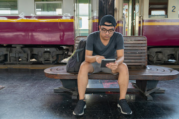 Fototapeta na wymiar Young backpacker man sitting and using tablet at railway, Travel concept