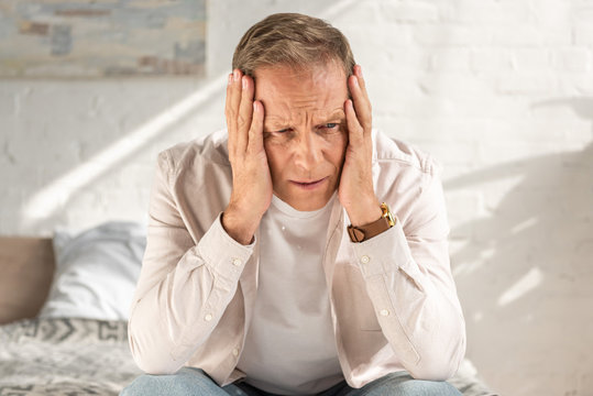 Disappointed man with hands near head sitting on bed - Powered by Adobe