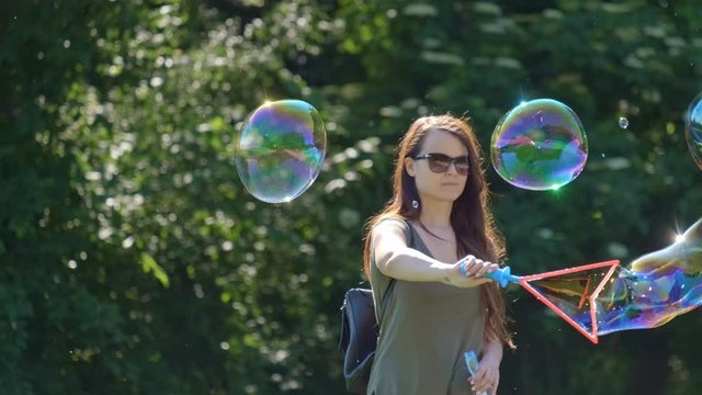 Pretty woman making Colorful Big shimmering Soap Bubbles in the forest. Background Green Trees. Slow Motion. Prores 10Bit mov. Happiness moment.