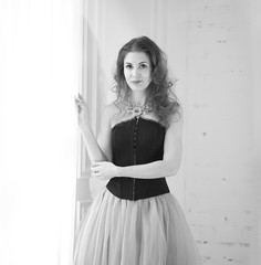 black and white portrait of a stylish model, girl in a tulle skirt and black corset is standing near the floor window. Beauty and fashion. Interior Design. Decor