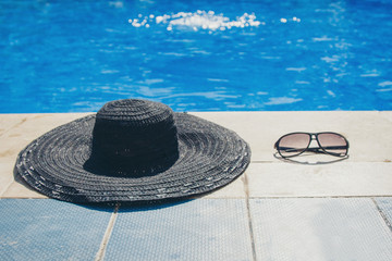 Fototapeta na wymiar sunglasses and a black hat on a stone slab by the pool close-up. concept of promotional accessories, clothing, beach holiday