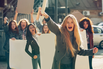 Young woman screaming in front of people protesting about women's rights and equality on the street. Meeting about problem in workplace, male pressure, domestic abuse, harassment. Copyspace.