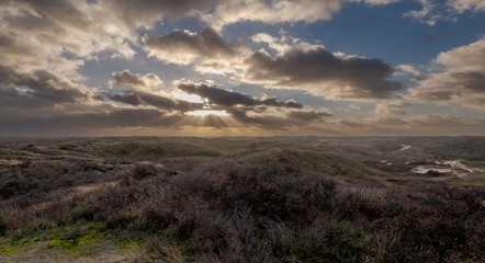 Sun rays through the heavy cloud cover above panoramic view of dune landscape