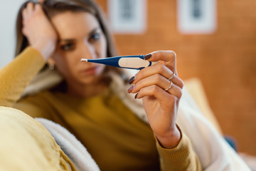 Young woman with cold and flu measuring her temperature