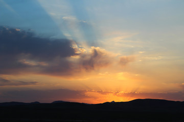 Sunrise shines reflected on golden clouds behind the mountains.