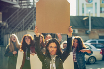 Young woman with blank poster in front of people protesting about women's rights and equality on...