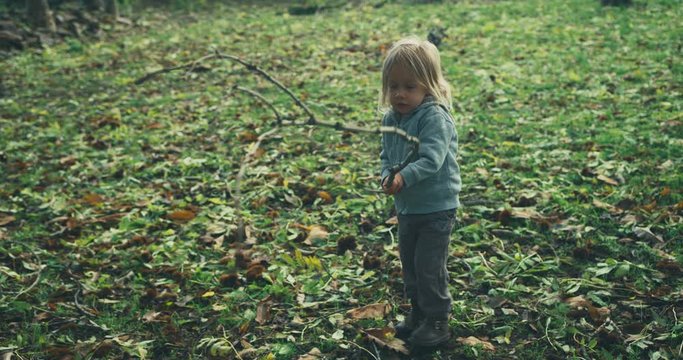 Little toddler waving a big stick in the woods