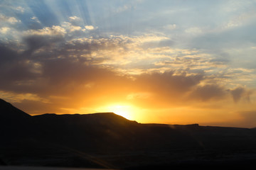 Naklejka na ściany i meble Sunrise shines reflected on golden clouds behind the mountains.