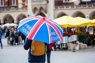 Fototapeta Free tour on a Cracow market square, a UK english guide with a united kingdom flag umbrella seen from the back. Local free of charge tourist guides. Tourism, travelling for england residents concept obraz