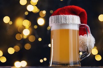 Christmas beer ale mug in Santa hat on dark background with bokeh garland. Craft beer
