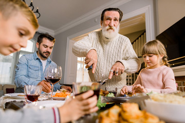 Happy grandfather cutting turkey for family on thanksgiving or christmas dinner