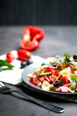 Traditional salad with pasta farfalle, ham, pepper and herbs on a dark plate on a dark background copy space