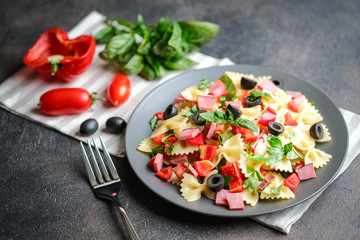 Traditional salad with pasta farfalle, ham, pepper and herbs on a dark plate on a dark background copy space