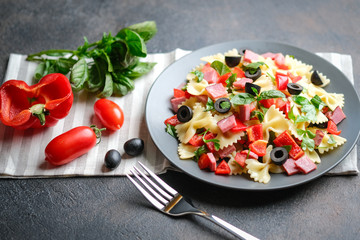 Traditional salad with pasta farfalle, ham, pepper and herbs on a dark plate on a dark background copy space