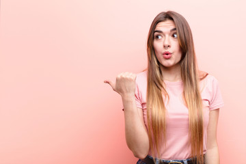young pretty woman looking astonished in disbelief, pointing at object on the side and saying wow,...