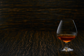 Full glass of cognac on a wooden table, selective focus with copy space.