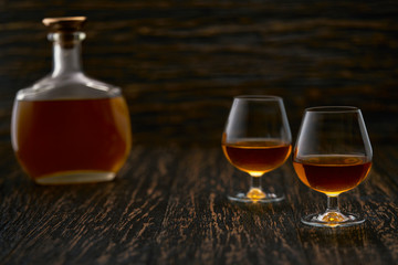 Two glasses of brandy or cognac and bottle on a wooden table.
