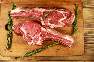 Raw fresh beef rib eye steaks on bone with spices and rosemary on wooden table. Top view