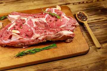 Raw fresh beef rib eye steak on bone with spices, garlic and rosemary on wooden table