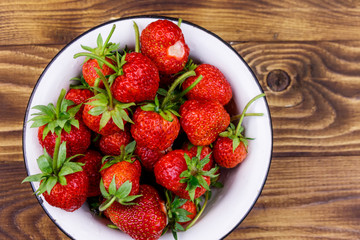 Fresh ripe strawberry in white bowl on a wooden table. Top view
