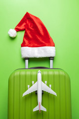 Flat lay of luggage with red santa hat and small commercial aircraft abstract on green.