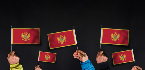 Fototapeta na wymiar Hands holds flags of Montenegro on dark background