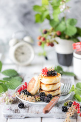 Homemade pancakes with berries, the blackberries, the honey on the plate, a branch of a BlackBerry alarm clock on white wooden background