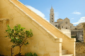 Fototapeta premium Matera alley with lemon plant and church. A Mediterranean courtyard with leaves of a small tree blowing in the wind.