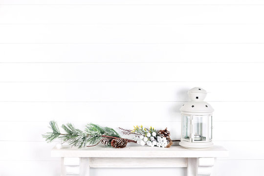white wall in a room with a mantelpiece, spruce branches, cones and a lantern
