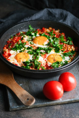 Traditional  shakshuka with eggs, tomato, and parsley in a iron pan on a dark background
