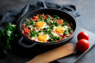 Traditional  shakshuka with eggs, tomato, and parsley in a iron pan on a dark background