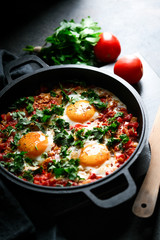 Traditional  shakshuka with eggs, tomato, and parsley in a iron pan on a dark background