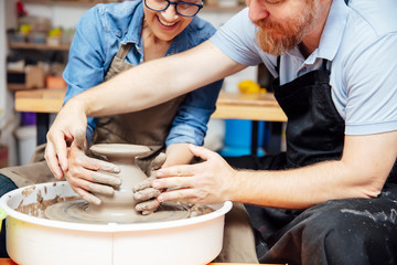 Senior woman spinning clay on a wheel with teacher at pottery class