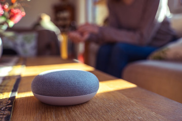 Obraz na płótnie Canvas voice controlled smart speaker with a woman woman in the background in a interior home environment. Smart AI speaker concept 