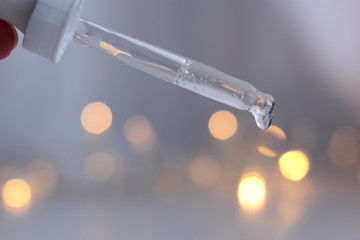 Closeup of a pipette with clear serum on a white background with fairy lights. Concept of winter skincare. 