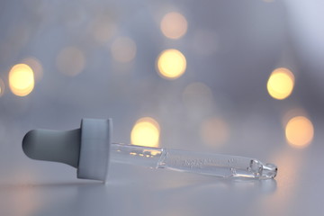 Closeup of a pipette with clear serum on a white background with fairy lights. Concept of winter skincare. 