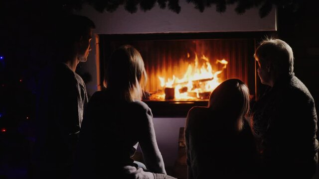 Family resting by the fireplace, watching the fire in the dark