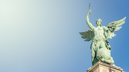 Fototapeta na wymiar Banner with top roof statue of sensual Renaissance Era angel with wings in front of blue sky with direct light in Vienna, Austria, and copy space, details, closeup