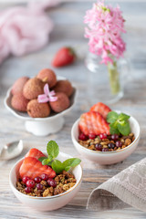 Spring Breakfast with granola and fresh strawberries and lychee and flowers on wooden background.