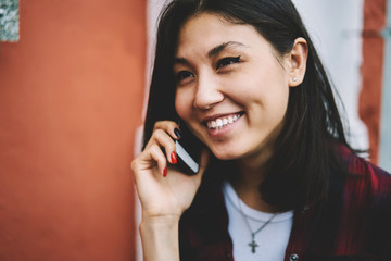 Concept of modern technology and communication in roaming, joyful brunette hipster girl 20s communicated with friend via application on contemporary mobile phone during positive call outdoors