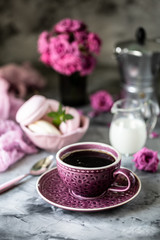 Cup of coffee for Breakfast with marshmallows in the form of macaroon cakes in a black bowl on a dark table and with flowers in a glass