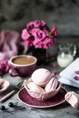 Cup of coffee for Breakfast with marshmallows in the form of macaroon cakes in a black bowl on a dark table and with flowers in a glass