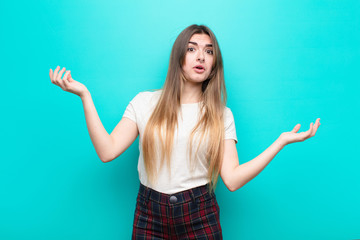 young pretty woman shrugging with a dumb, crazy, confused, puzzled expression, feeling annoyed and...