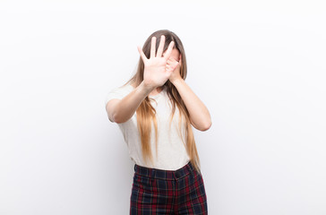 young pretty woman covering face with hand and putting other hand up front to stop camera, refusing...