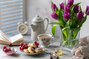 Cottage cheese dessert, cheesecakes on the table with a bouquet of tulips, clocks and fruit on a wooden table by the window.