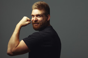 Fabulous at any age. Portrait of charismatic muscular 30-year-old man standing over dark gray background showing bicep. Perfect haircut. Rocker, biker, hipster style. Copy-space. Studio shot