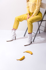 cropped view of woman sitting near yellow bananas on white